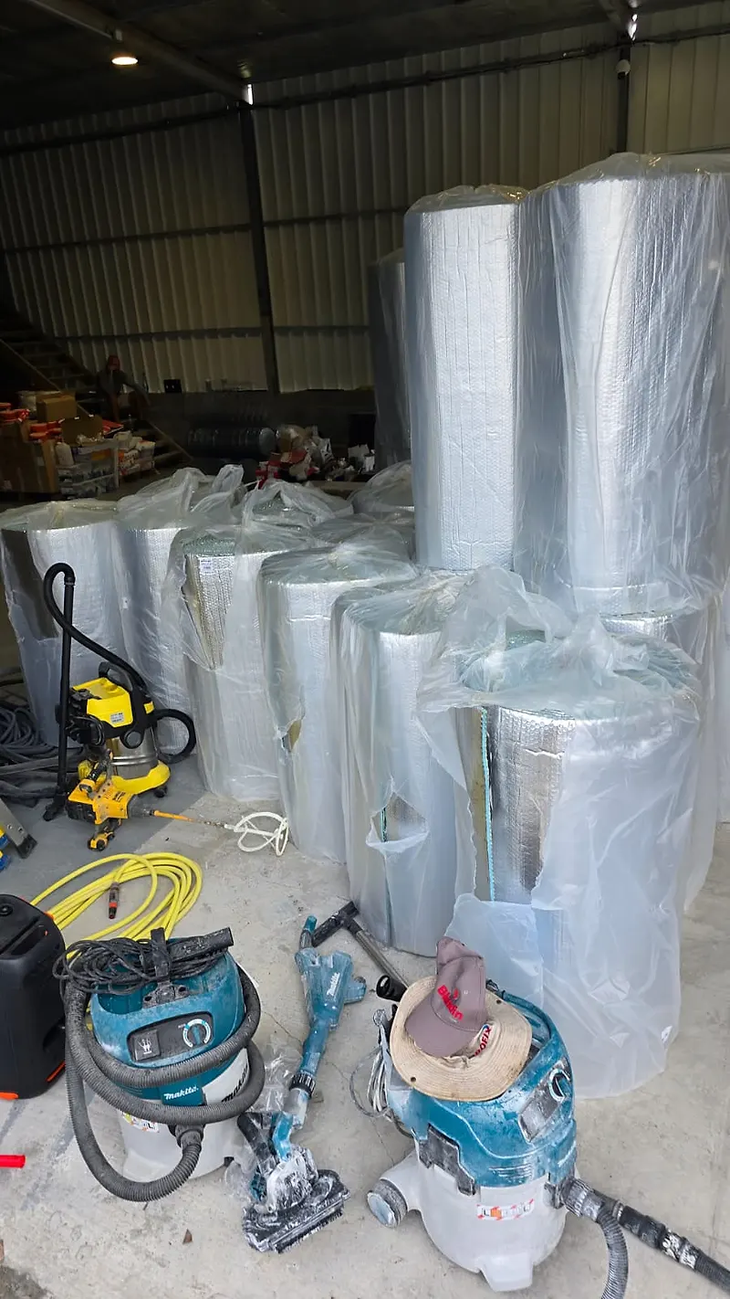 Rouleaux de R'BULL Pro 13 sous film plastique, stockés sur un chantier aux Antilles avec les aspirateurs et l'outillage des poseurs